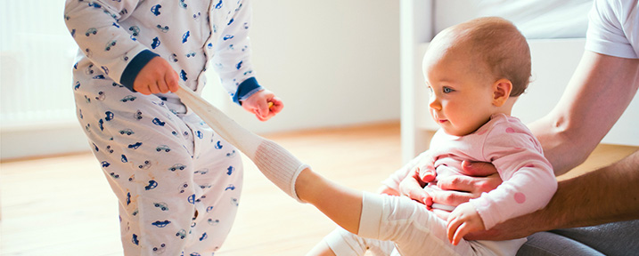 child pulling sock off of baby's foot sitting on hardwood floors